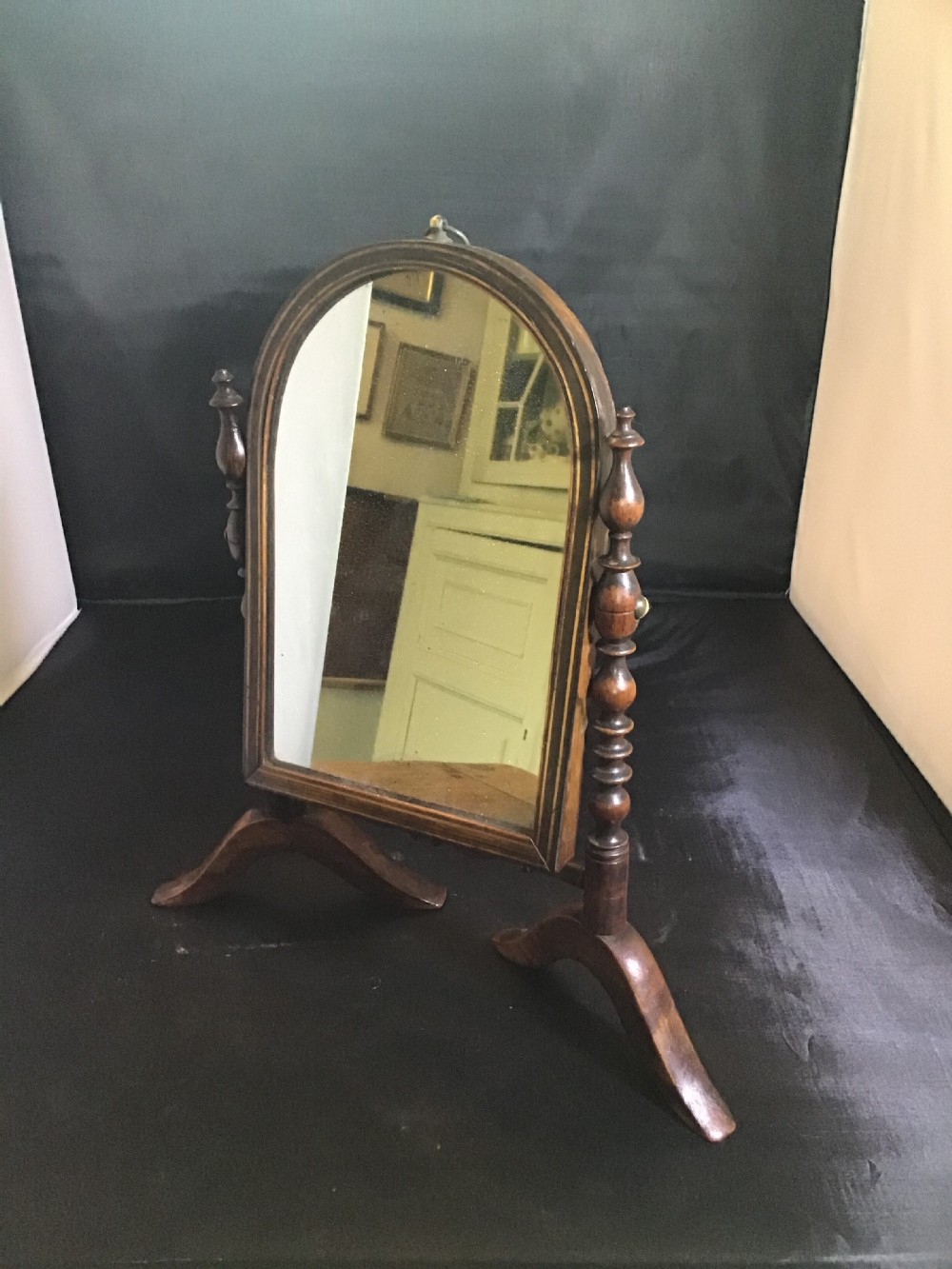 An antique mahogany swing toilet mirror featuring an arched wooden frame, turned support posts, and splayed legs against a dark background. View IV