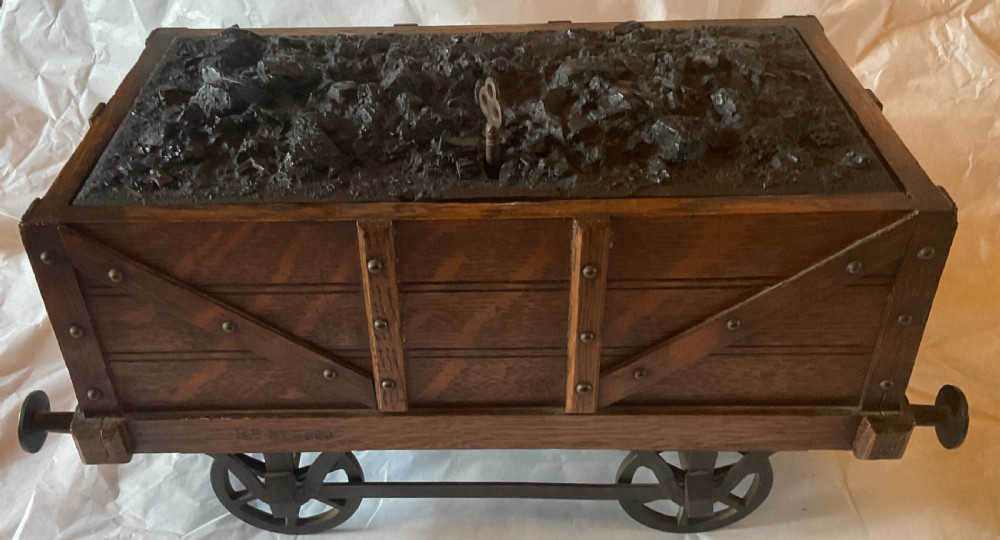 An antique Victorian oak cigar humidor constructed in the shape of a railway coal wagon with metal wheels, side bracing, and faux coal lining the top.