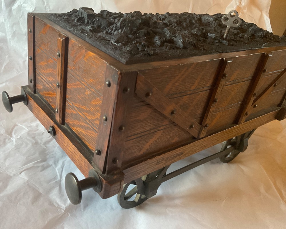 An antique Victorian oak cigar humidor constructed in the shape of a railway coal wagon with metal wheels, side bracing, and faux coal lining the top. View II