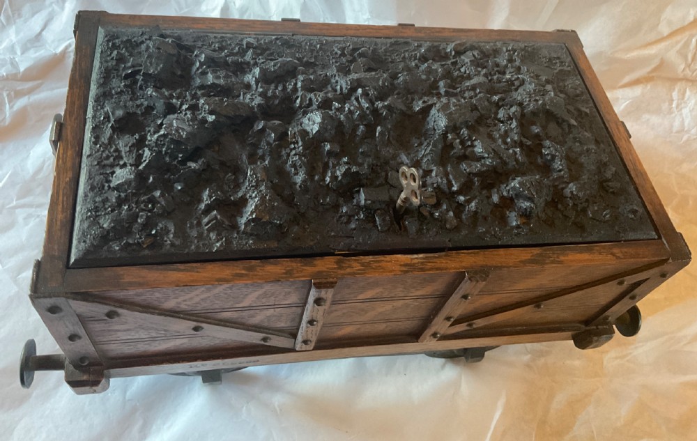 An antique Victorian oak cigar humidor constructed in the shape of a railway coal wagon with metal wheels, side bracing, and faux coal lining the top. View V