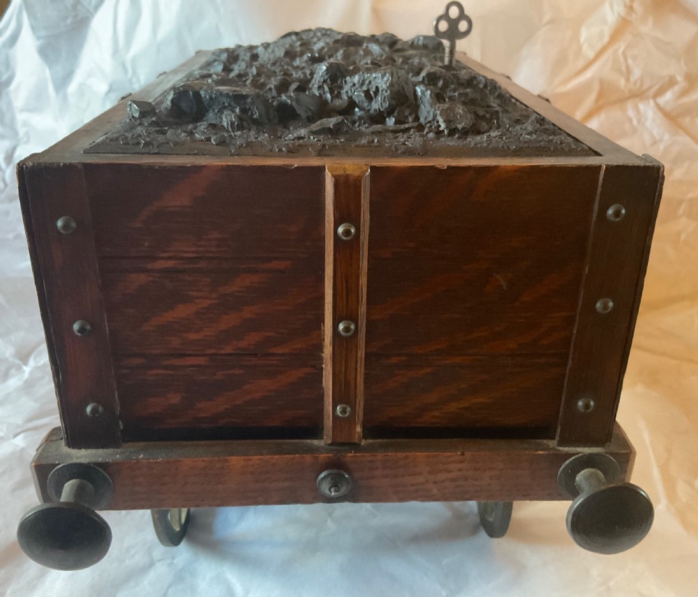 An antique Victorian oak cigar humidor constructed in the shape of a railway coal wagon with metal wheels, side bracing, and faux coal lining the top. View VI
