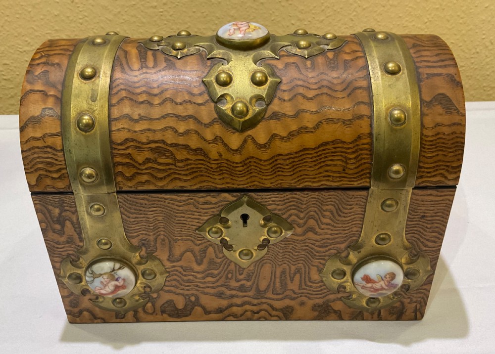 A Victorian domed walnut casket featuring brass strapwork, decorative studs, keyhole escutcheon, and porcelain cabochons with painted cherubs.