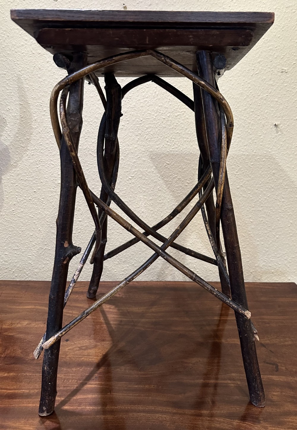 A dark brown wooden side table featuring a square top with relief floral carving supported by a rustic twig base. View II