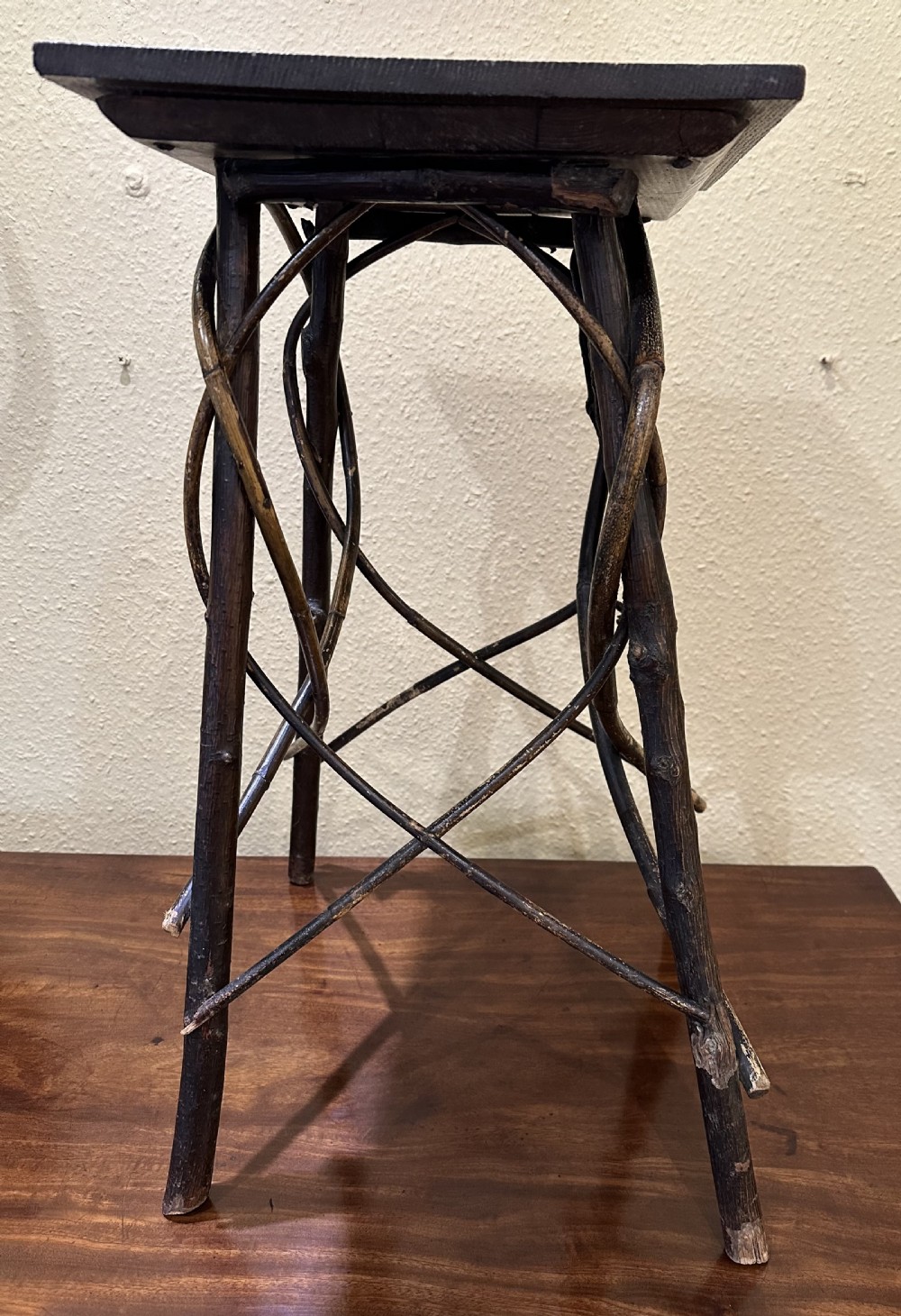 A dark brown wooden side table featuring a square top with relief floral carving supported by a rustic twig base. View III