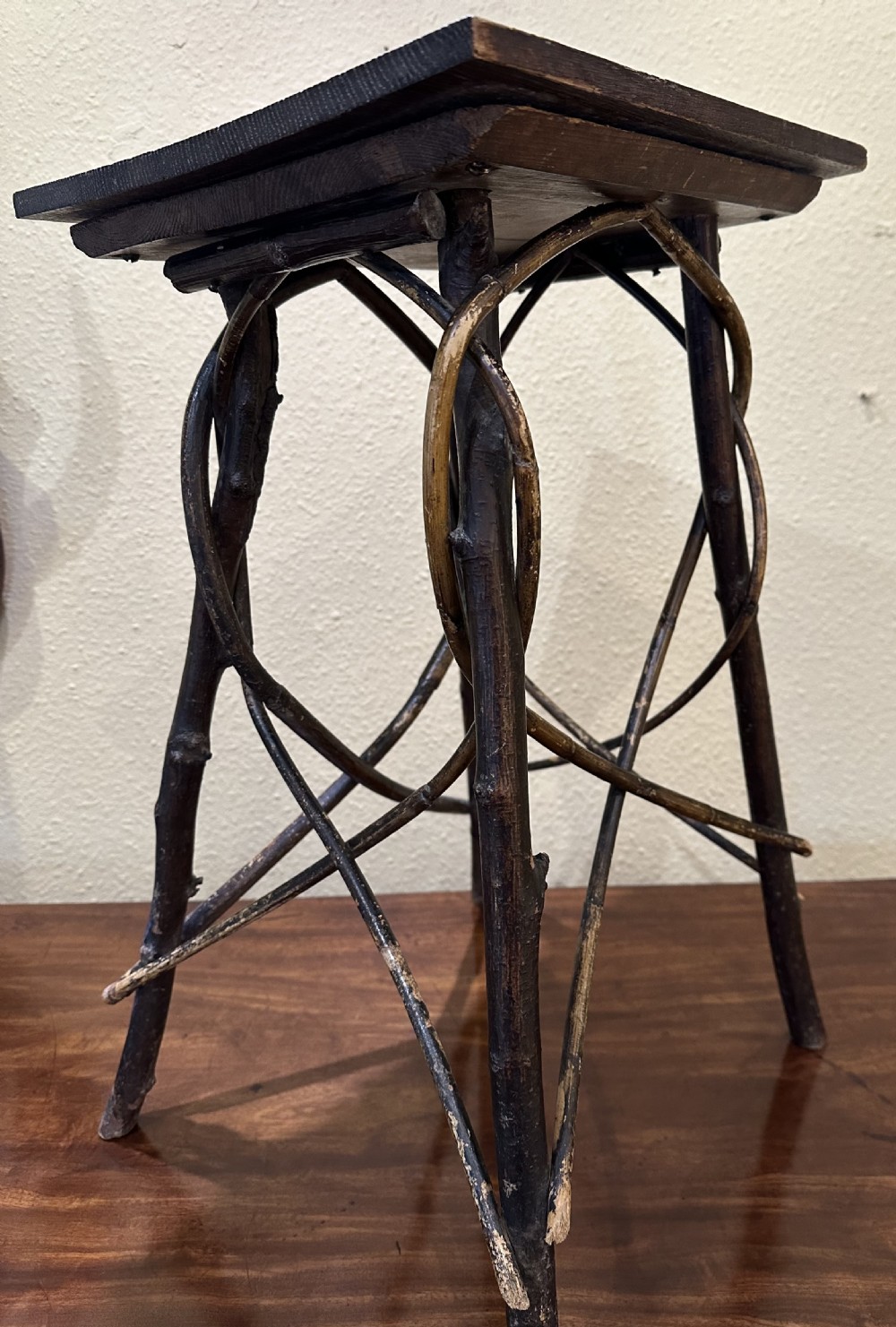A dark brown wooden side table featuring a square top with relief floral carving supported by a rustic twig base. View VI