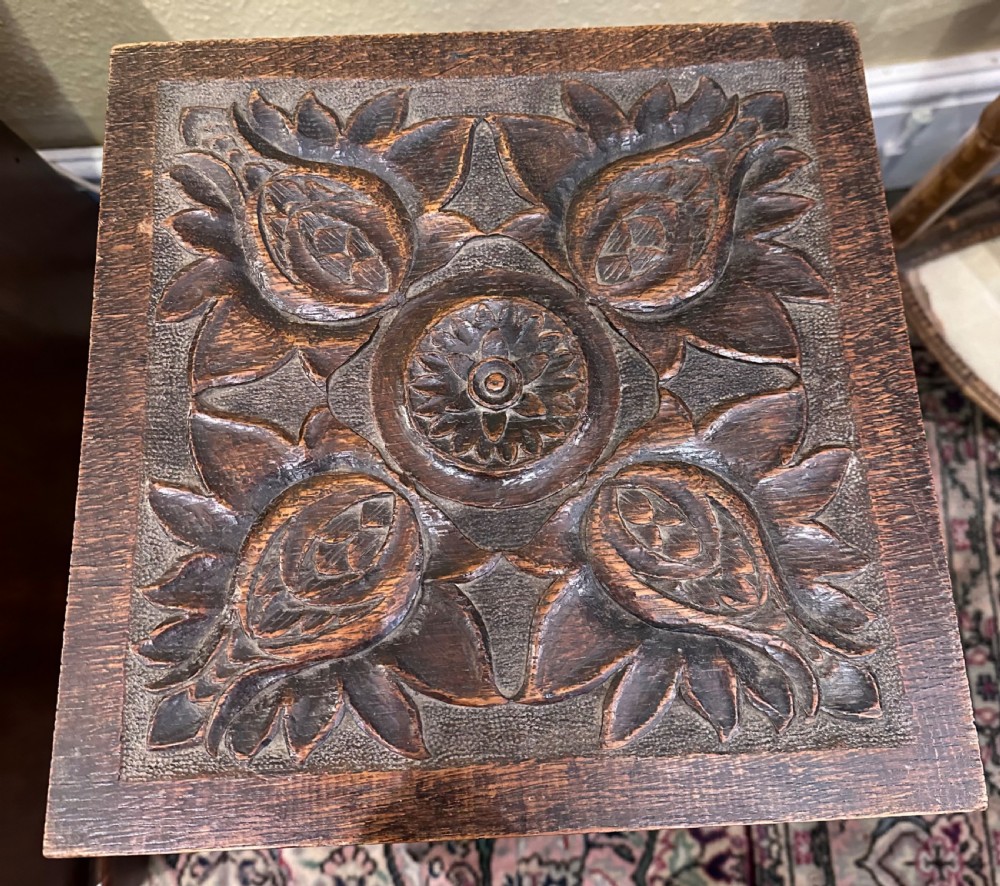 A dark brown wooden side table featuring a square top with relief floral carving supported by a rustic twig base. View VII