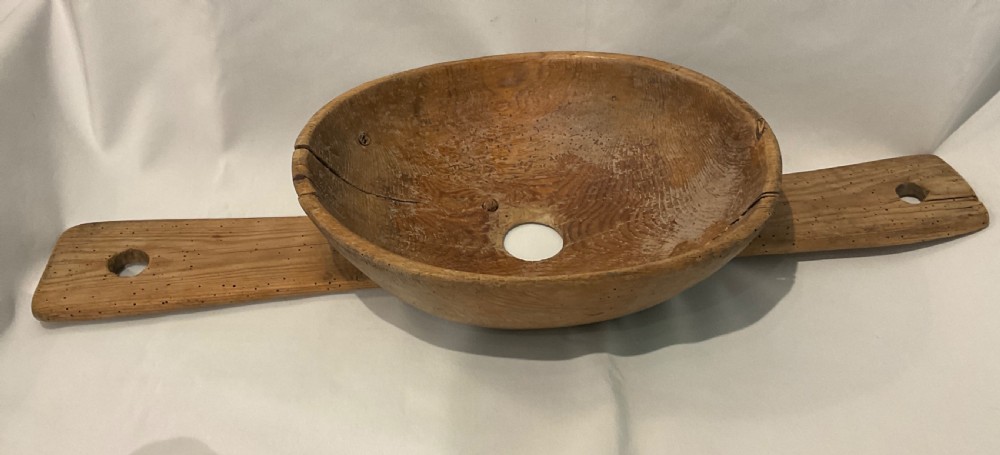 A hand-carved primitive wooden milk strainer featuring a central round bowl with a bottom drainage hole set across a flat wooden support board.