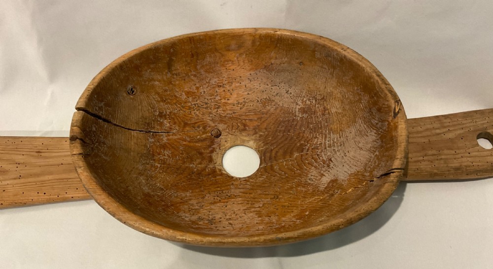 A hand-carved primitive wooden milk strainer featuring a central round bowl with a bottom drainage hole set across a flat wooden support board. View II
