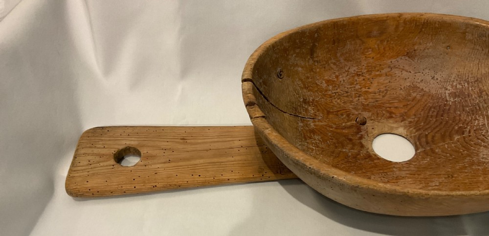 A hand-carved primitive wooden milk strainer featuring a central round bowl with a bottom drainage hole set across a flat wooden support board. View III