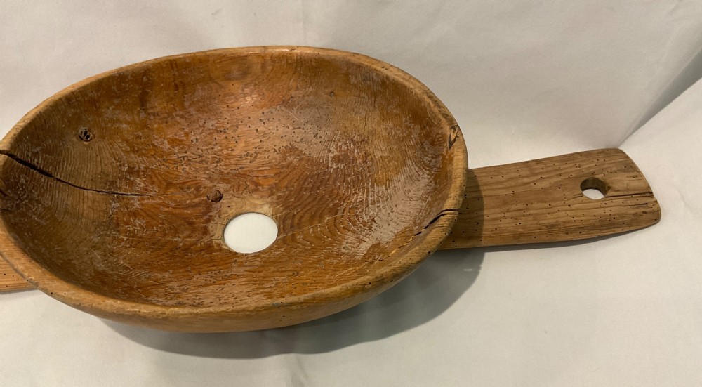 A hand-carved primitive wooden milk strainer featuring a central round bowl with a bottom drainage hole set across a flat wooden support board. View IV