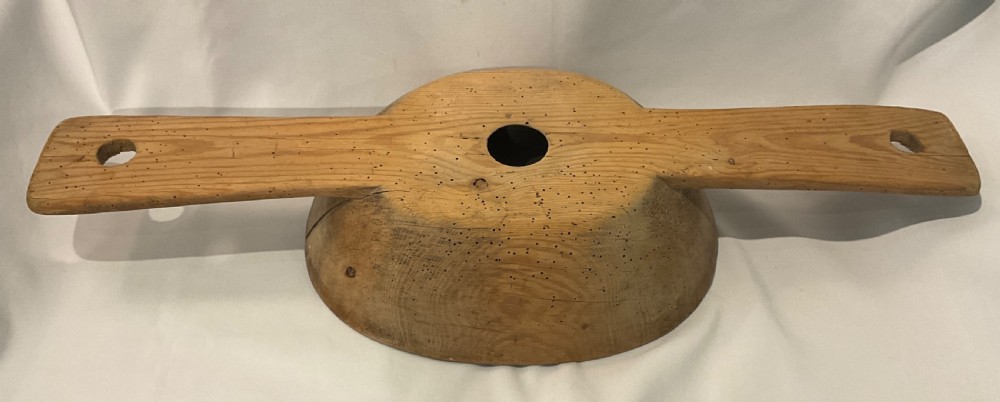A hand-carved primitive wooden milk strainer featuring a central round bowl with a bottom drainage hole set across a flat wooden support board. View V