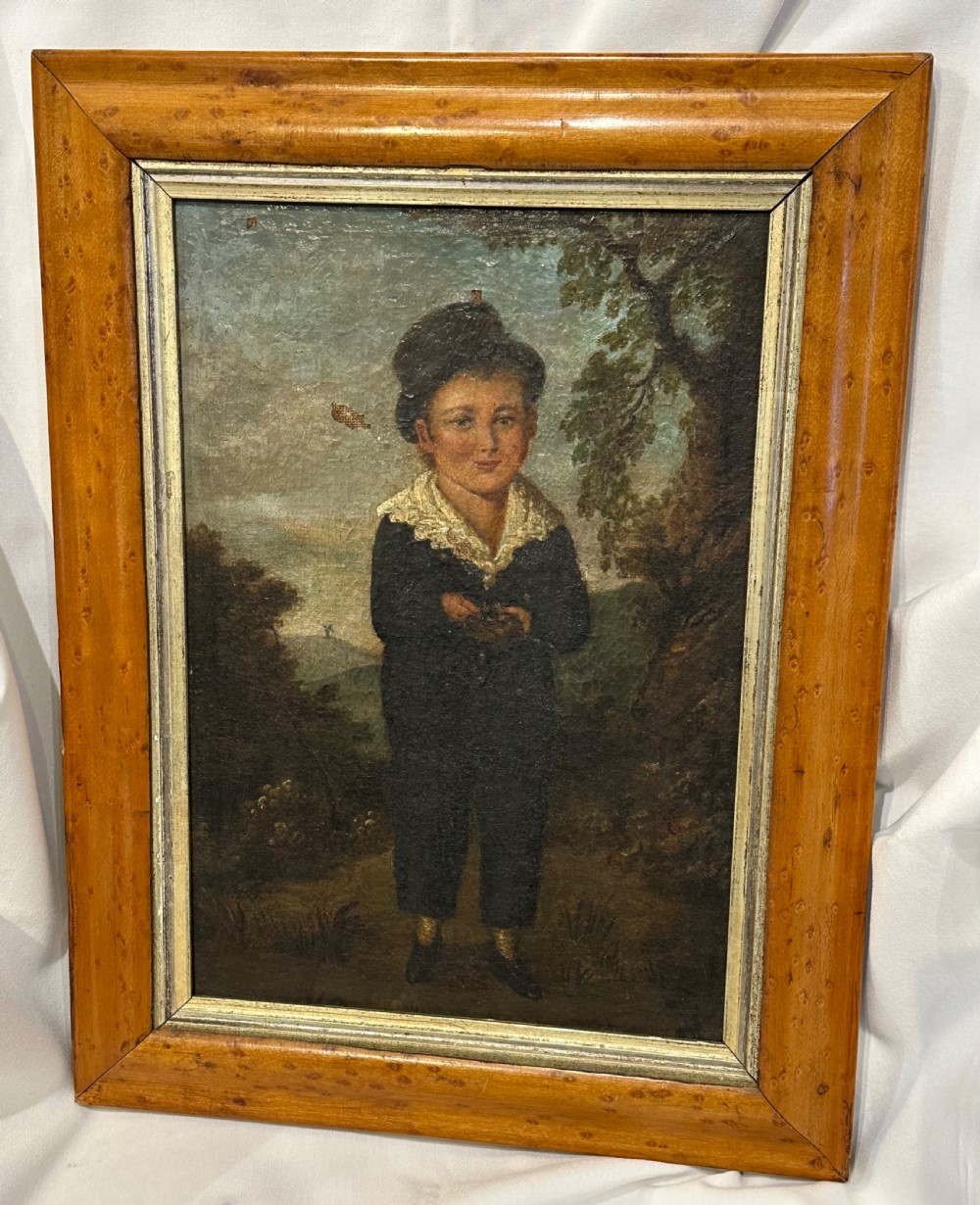 An antique naive oil painting depicting a young boy in dark attire holding a bird nest within a landscape setting, enclosed in a wooden frame.