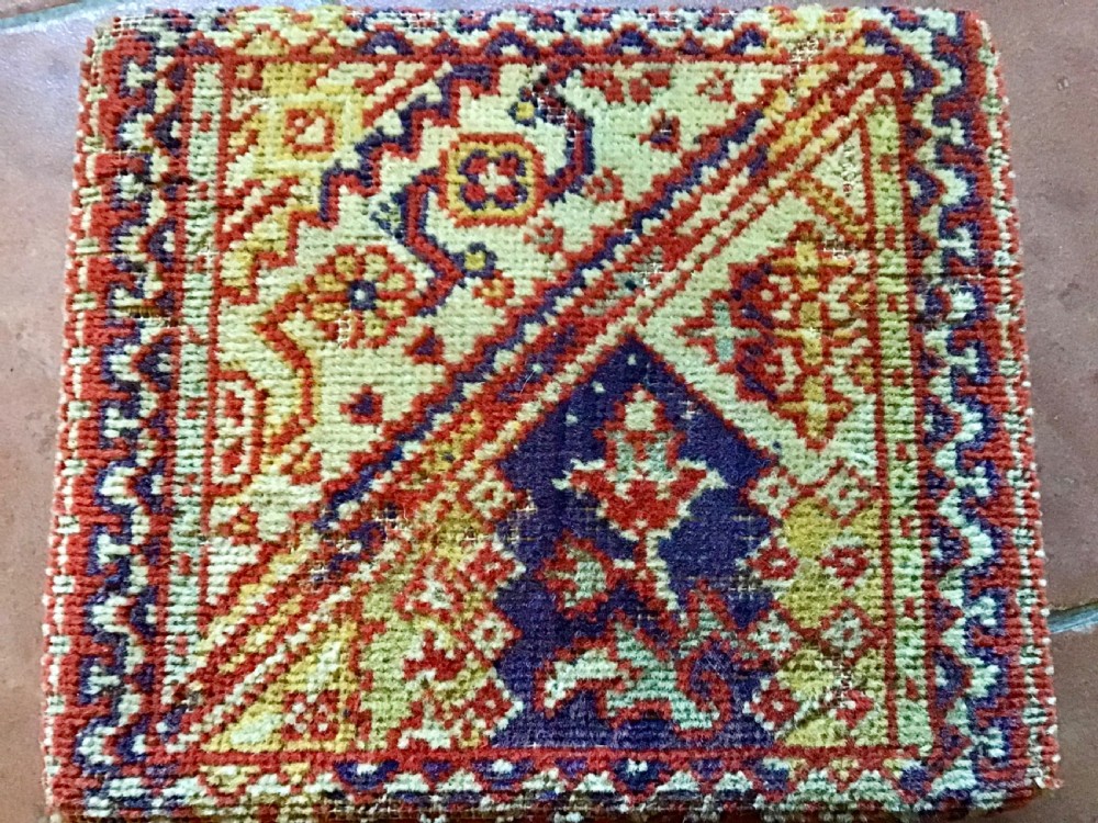 An antique Victorian carriage foot warmer featuring a square patterned carpet top with stud detailing, a wooden base with turned feet, and a metal carry handle. View VII