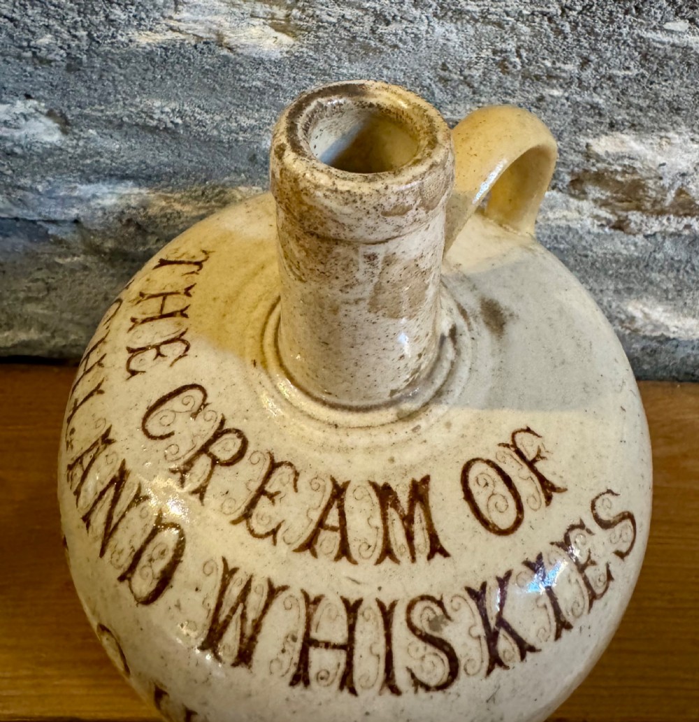 A cream glazed Victorian stoneware whisky jug featuring brown transfer-printed typography and botanical decoration with a single side handle. View II