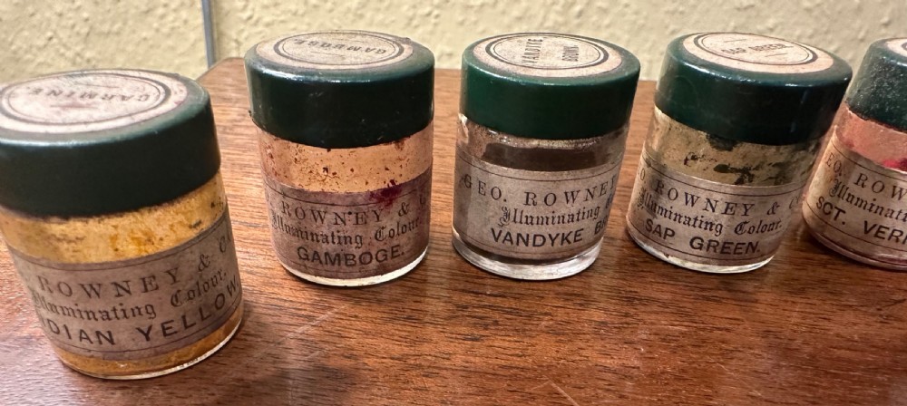 An open Victorian wooden artist box containing glass pigment jars, ceramic bowls, a brush, and an illustrated lid label for George Rowney and Company. View II