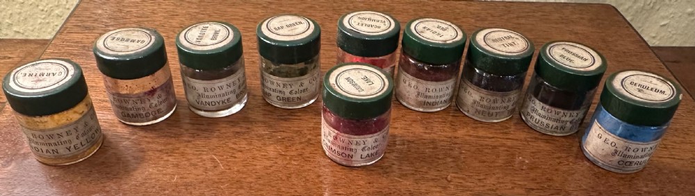 An open Victorian wooden artist box containing glass pigment jars, ceramic bowls, a brush, and an illustrated lid label for George Rowney and Company. View V