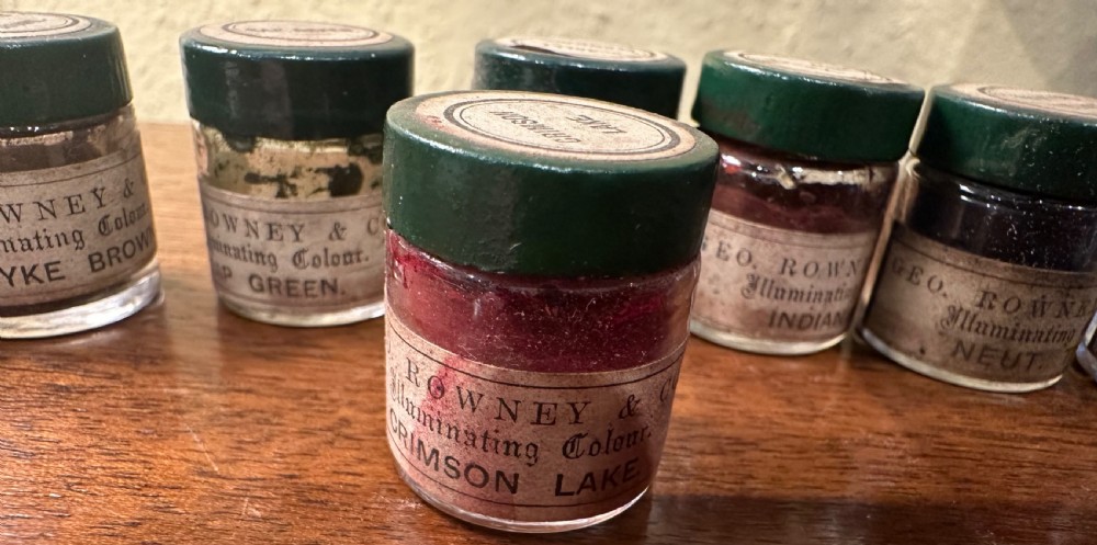 An open Victorian wooden artist box containing glass pigment jars, ceramic bowls, a brush, and an illustrated lid label for George Rowney and Company. View VIII