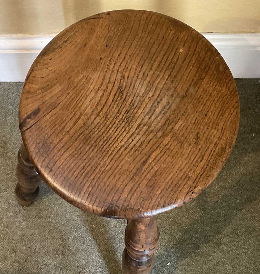 A dark stained wooden Windsor stool featuring a circular solid wood seat, four turned legs, and cross stretchers. View II