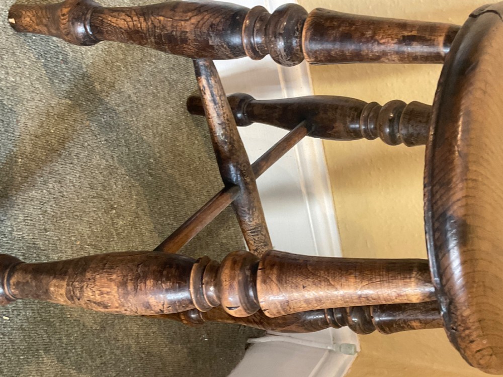 A dark stained wooden Windsor stool featuring a circular solid wood seat, four turned legs, and cross stretchers. View III