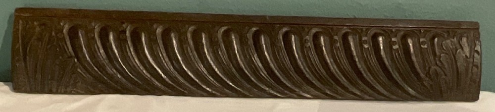 A long rectangular 17th-century carved dark oak frieze panel with repeating diagonal fluting and leaf end motifs. View V