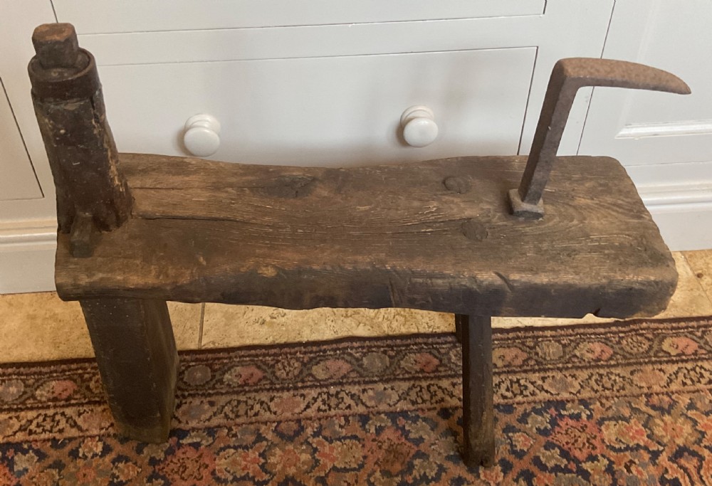 A rustic dark oak cobbler bench featuring a thick timber top with integrated iron tools and sturdy wooden leg supports.