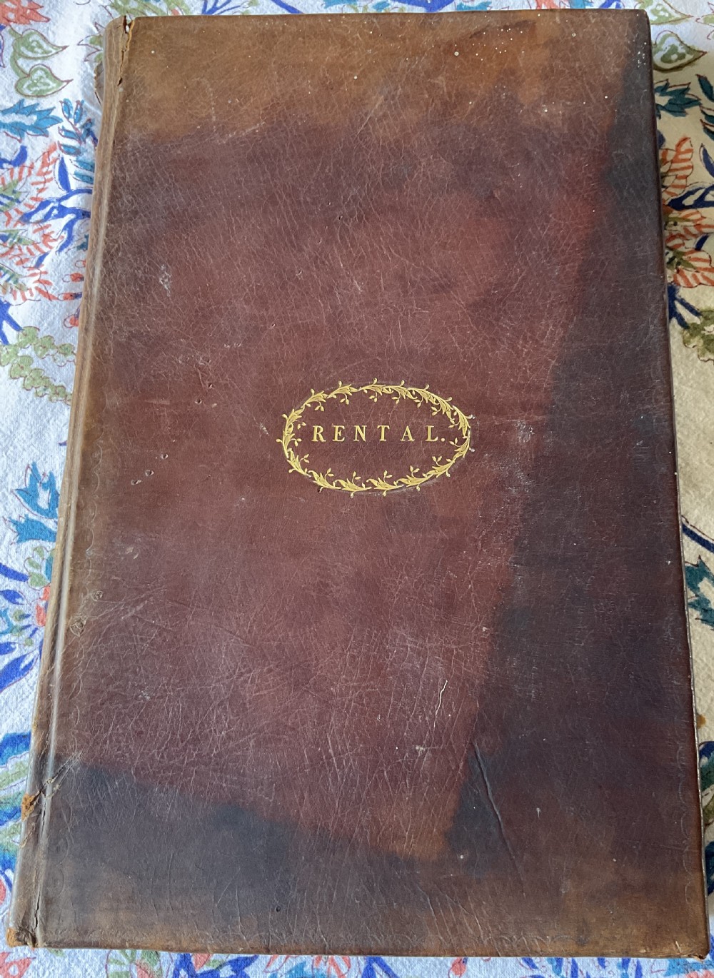 An 18th-century dark brown leather-bound ledger featuring a central gilt oval wreath cartouche with the word RENTAL stamped in gold.