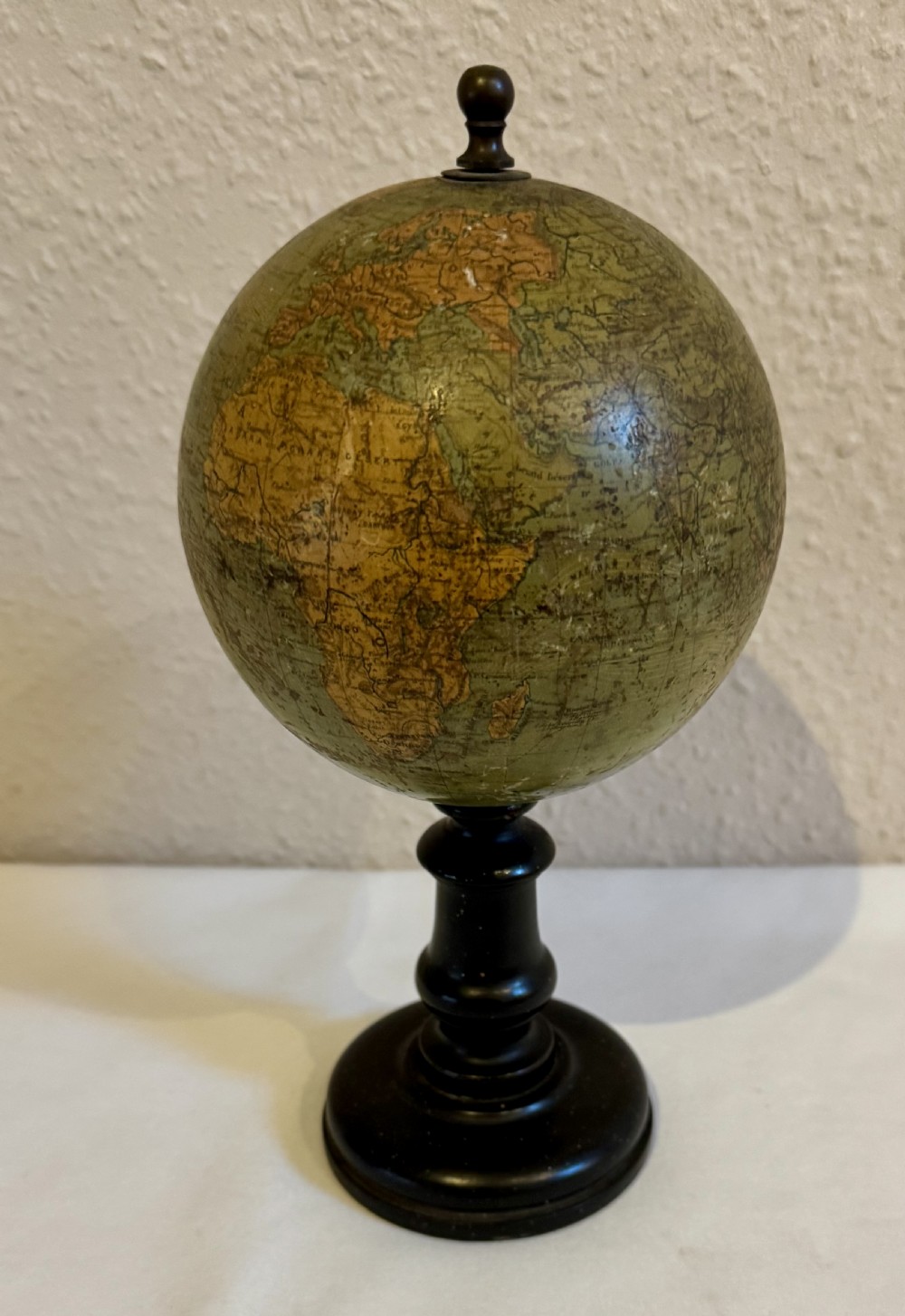 A small antique terrestrial globe featuring muted green and brown cartography mounted on a dark ebonised turned wooden stand with a finial top.