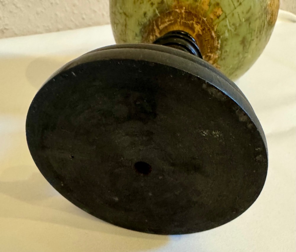 A small antique terrestrial globe featuring muted green and brown cartography mounted on a dark ebonised turned wooden stand with a finial top. View VI