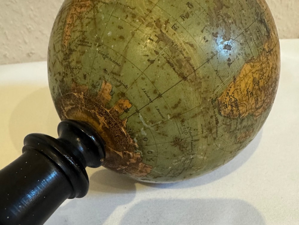 A small antique terrestrial globe featuring muted green and brown cartography mounted on a dark ebonised turned wooden stand with a finial top. View VII