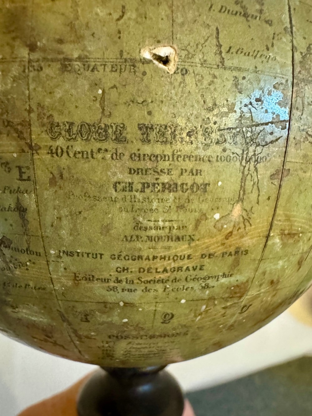 A small antique terrestrial globe featuring muted green and brown cartography mounted on a dark ebonised turned wooden stand with a finial top. View VIII
