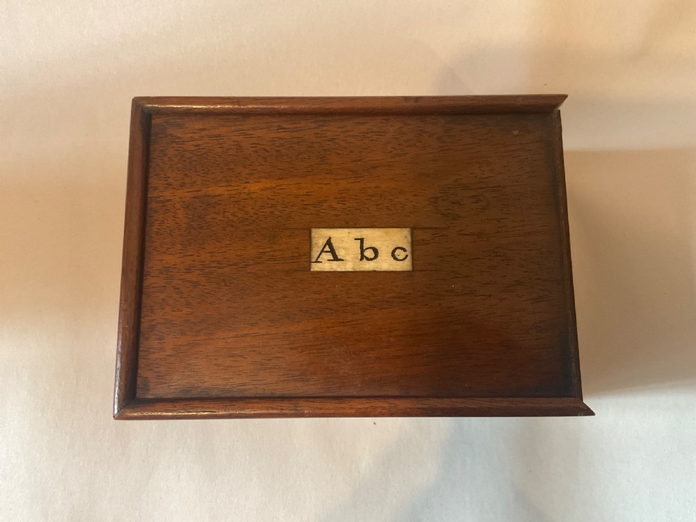 A mahogany box with a sliding lid featuring an inlaid bone plaque inscribed A b c, containing rectangular bone tiles stamped with black lettering. View II