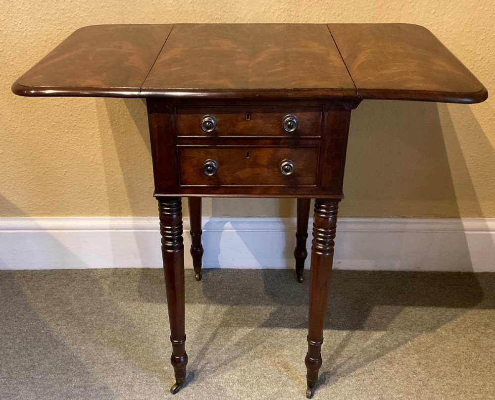 A Victorian mahogany work table featuring two drawers with brass pull knobs, side drop-leaf extensions, and slender turned legs on brass castors. View II