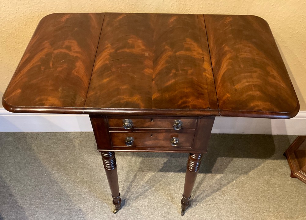 A Victorian mahogany work table featuring two drawers with brass pull knobs, side drop-leaf extensions, and slender turned legs on brass castors. View IV