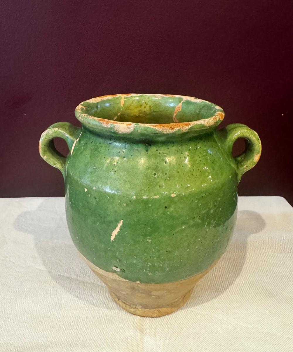 An antique French terracotta confit pot featuring a green glaze on the upper body, two loop handles, and an unglazed earthen base.