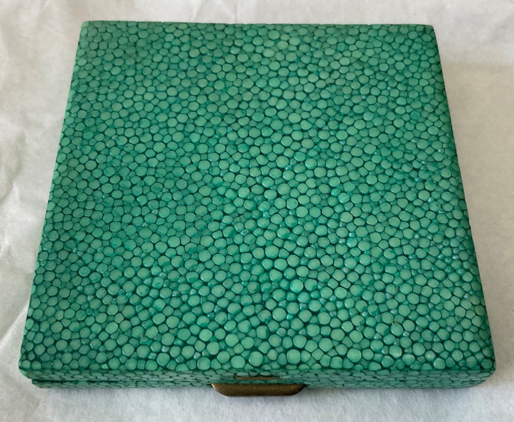 A square Art Deco vanity compact covered in green dyed shagreen with a brass catch.