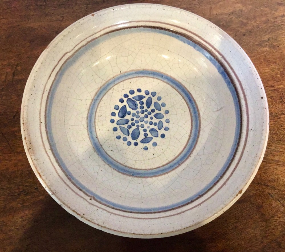 An antique round French tin-glazed earthenware bowl featuring a cream-coloured interior with blue circular lines and a central floral motif.