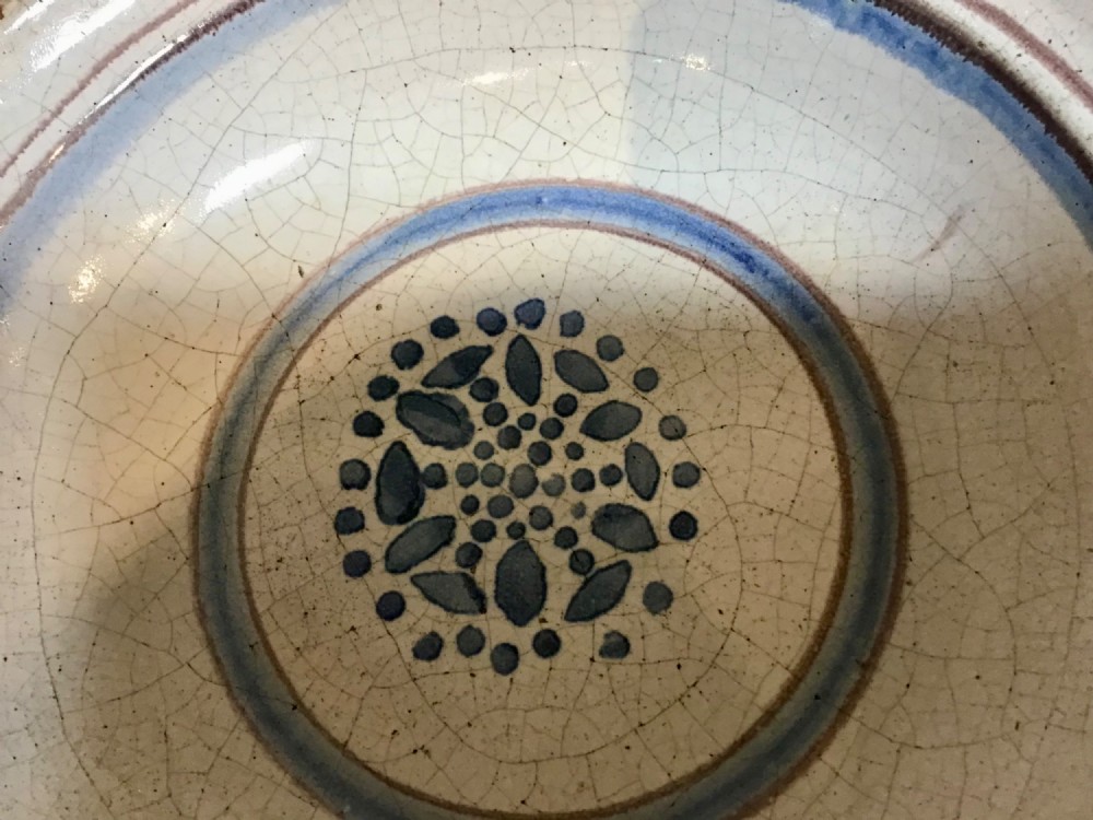 An antique round French tin-glazed earthenware bowl featuring a cream-coloured interior with blue circular lines and a central floral motif. View II
