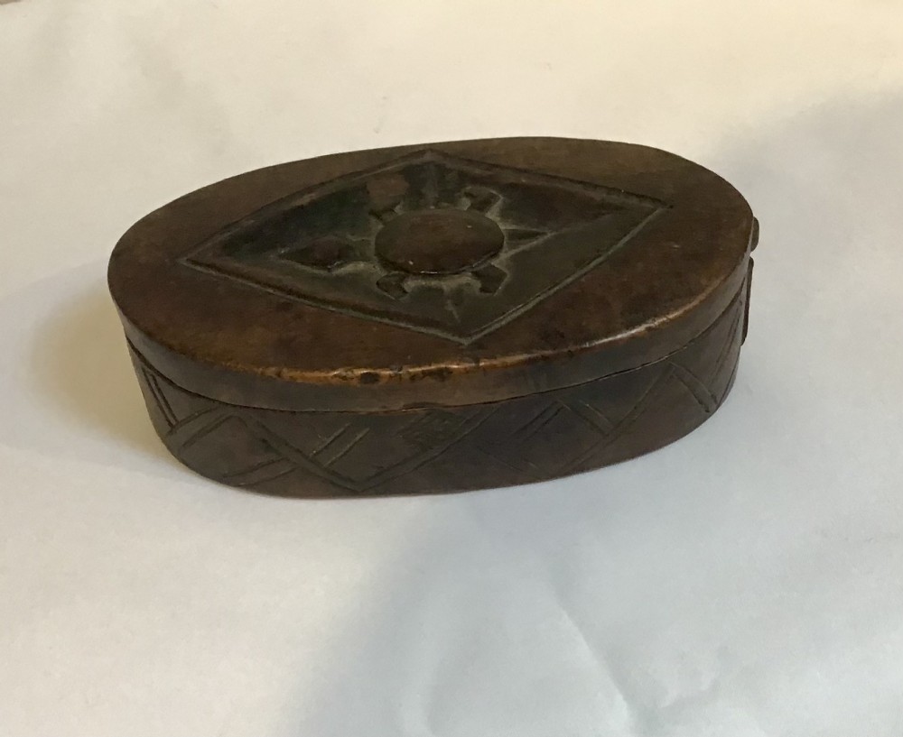 An oval hand-carved dark wood box featuring geometric relief patterns on the lid and sides.