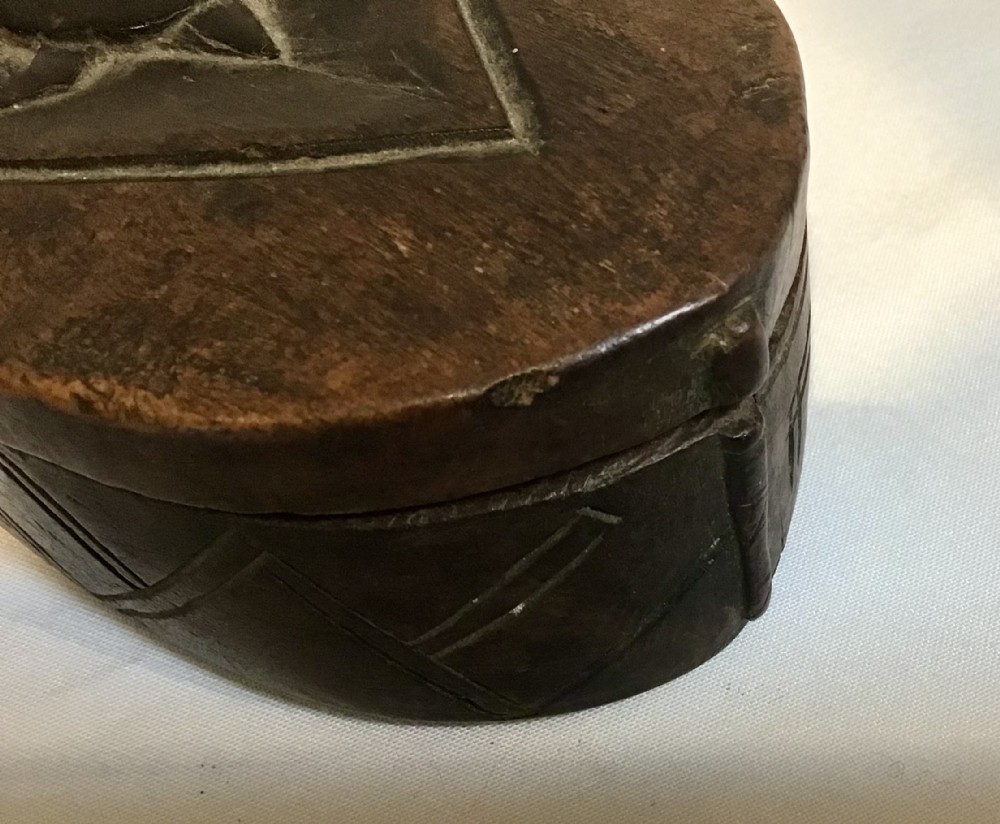 An oval hand-carved dark wood box featuring geometric relief patterns on the lid and sides. View II