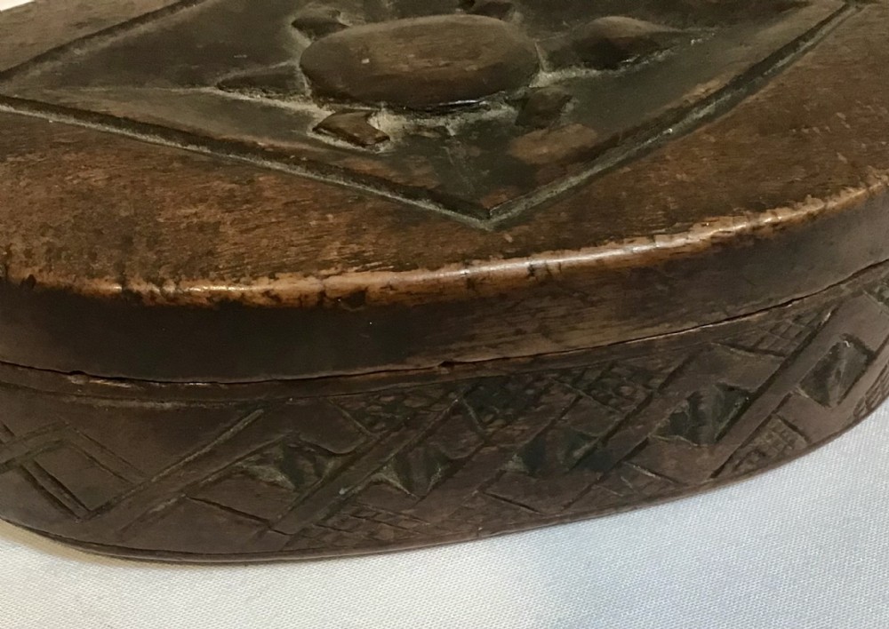 An oval hand-carved dark wood box featuring geometric relief patterns on the lid and sides. View III