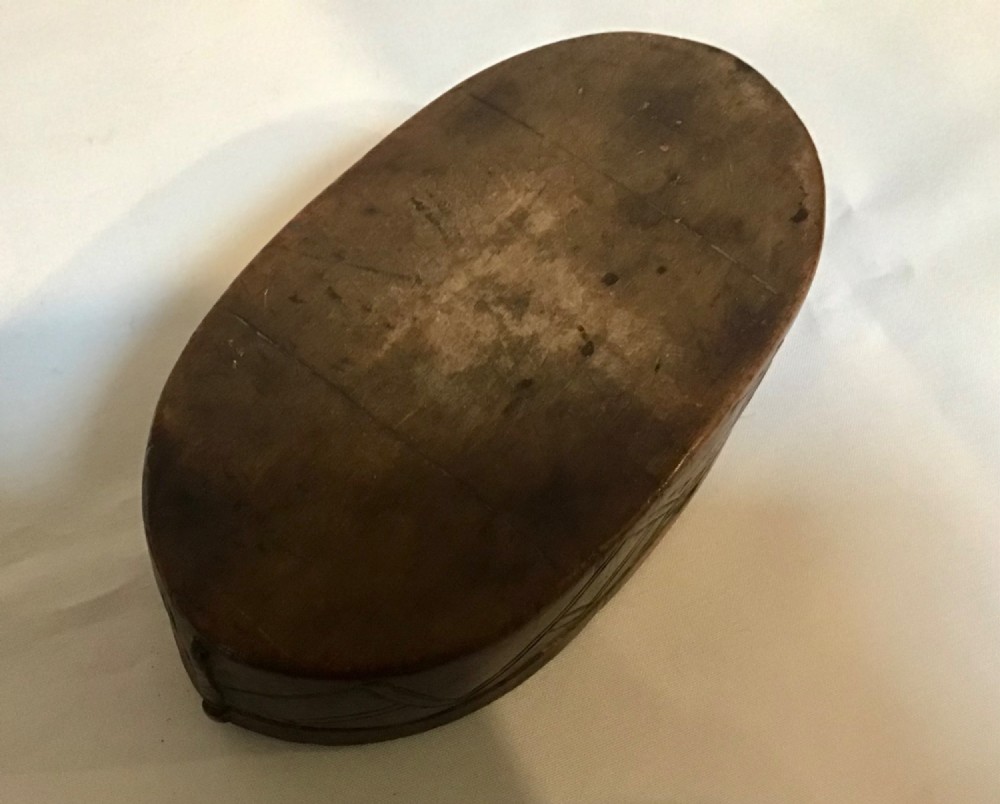 An oval hand-carved dark wood box featuring geometric relief patterns on the lid and sides. View V