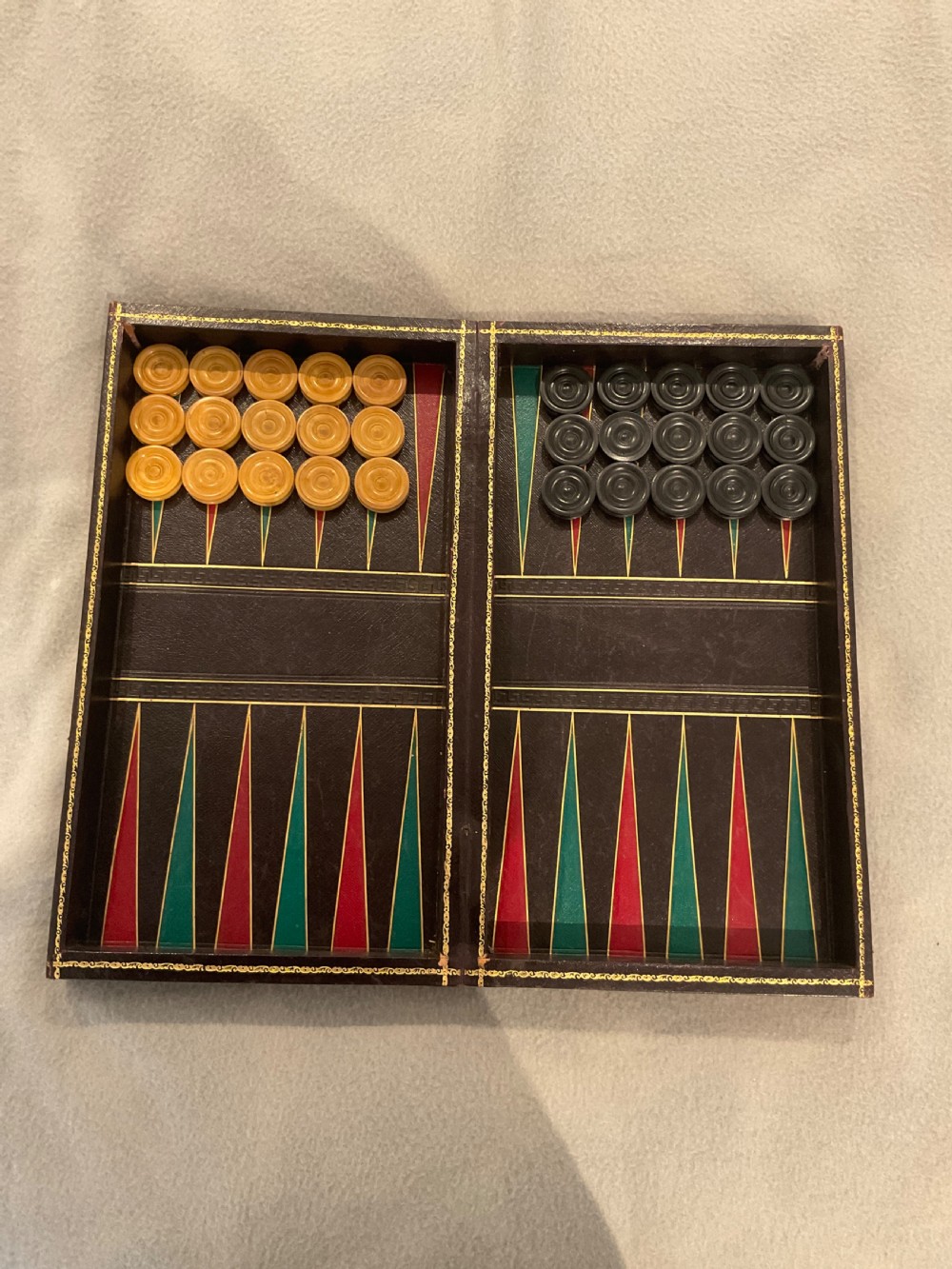An open dark brown leather games board disguised as a book, displaying red and green backgammon points with black and cream counters.