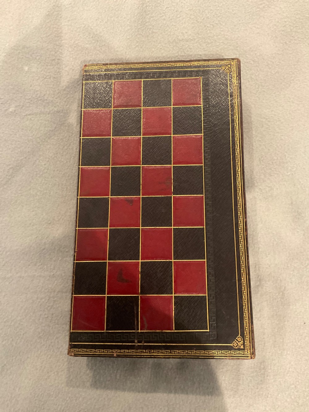 An open dark brown leather games board disguised as a book, displaying red and green backgammon points with black and cream counters. View V