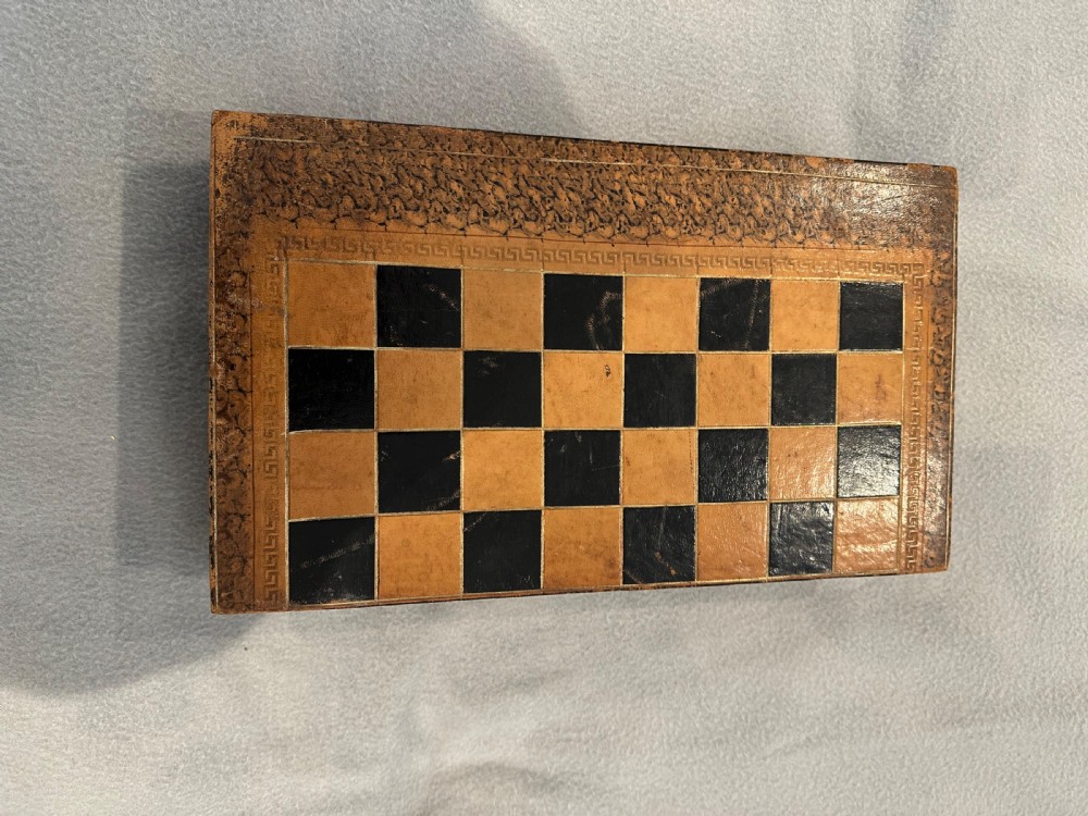 An antique closed leather-bound faux book games board decorated with a black and tan chequerboard pattern and gilt-tooled borders.