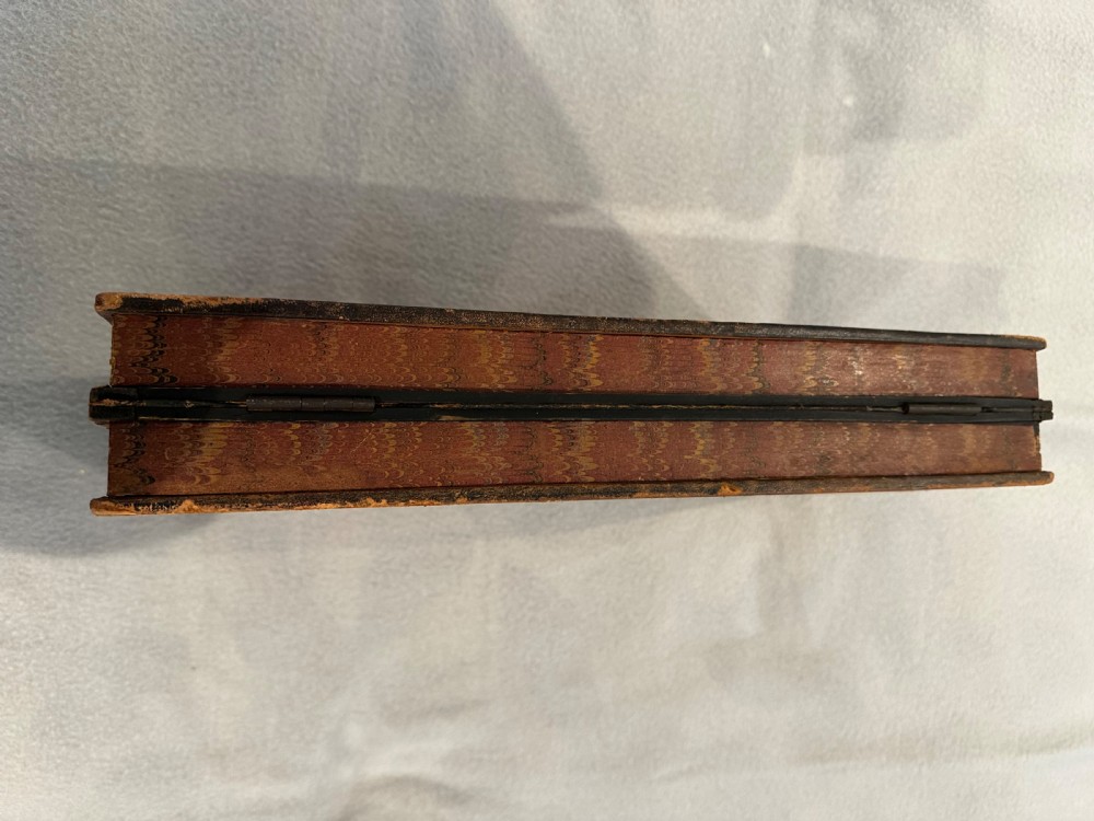 An antique closed leather-bound faux book games board decorated with a black and tan chequerboard pattern and gilt-tooled borders. View II
