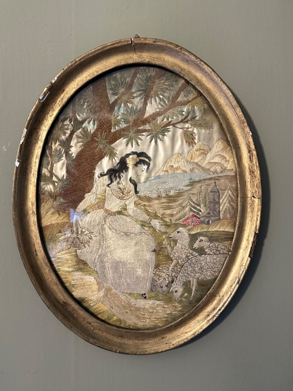 An oval Regency embroidered silk picture depicting a shepherdess and sheep under a tree within a gilded frame.