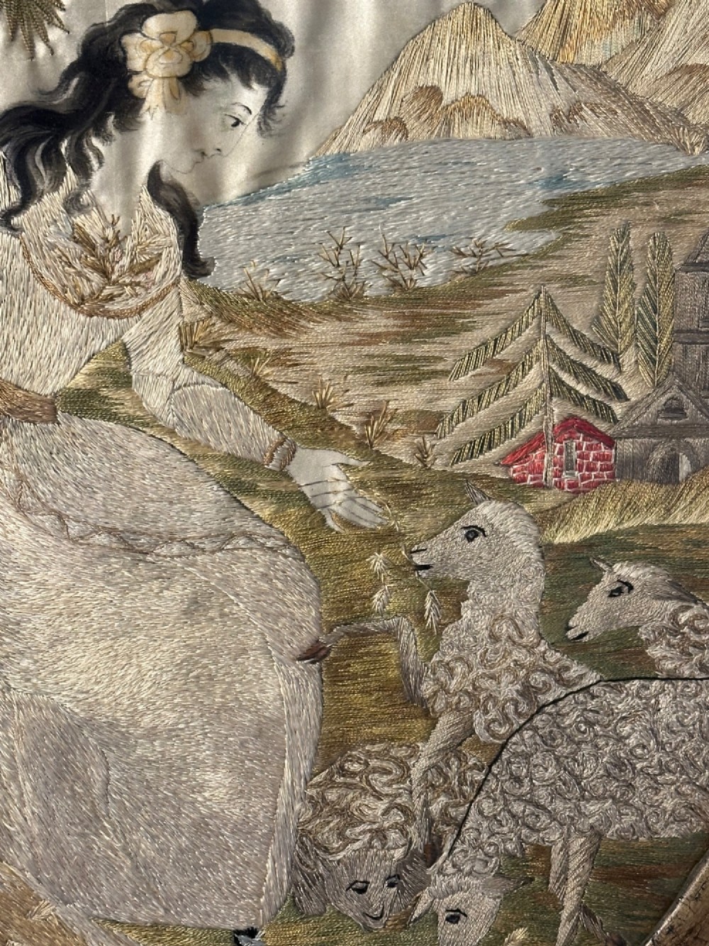 An oval Regency embroidered silk picture depicting a shepherdess and sheep under a tree within a gilded frame. View II