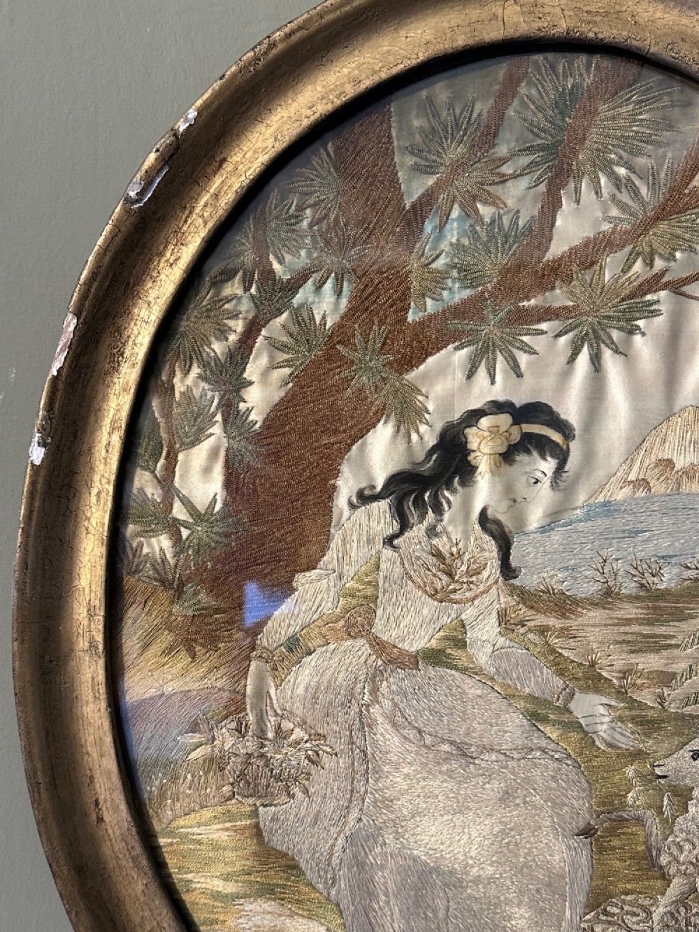 An oval Regency embroidered silk picture depicting a shepherdess and sheep under a tree within a gilded frame. View IV