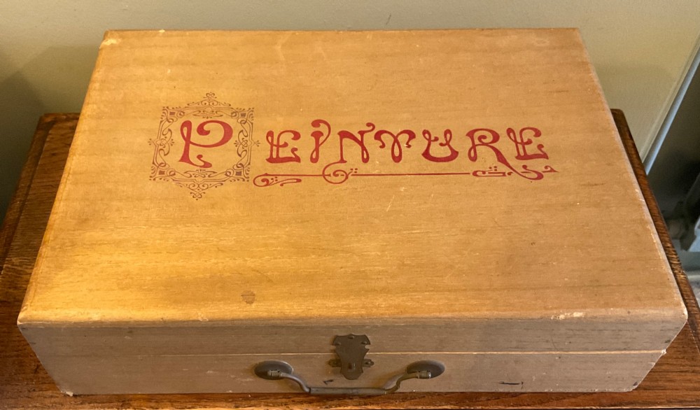 An open French beechwood artist paintbox displaying miniature wood easels, set squares, and velvet-lined compartments containing paint cakes and crayons. View II