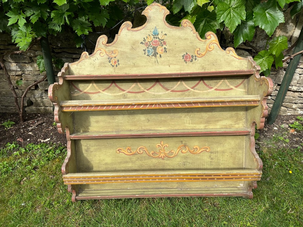 A sage green hand-painted wooden wall shelf unit featuring a decorative scalloped crest with floral motifs and three open display shelves with front retaining bars. View III
